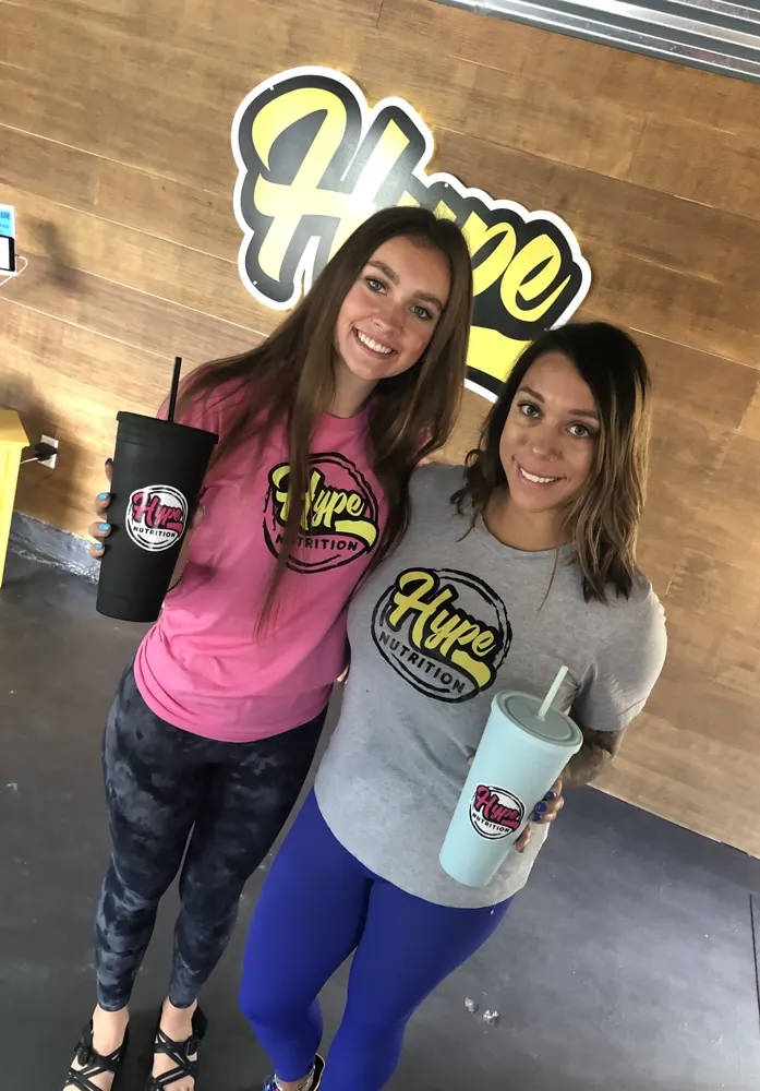 Two friends with their Hype drinks at the sign