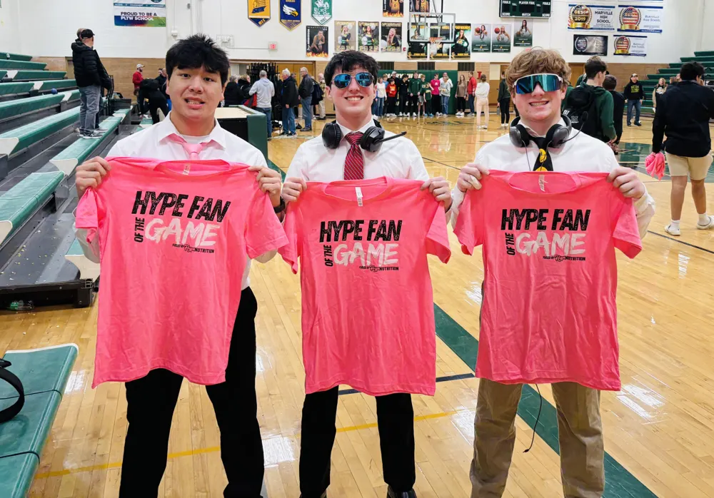Three Hype Fans of the Game holding their pink shirts at a basketball game